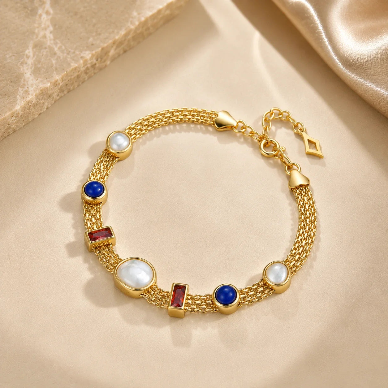 lumiere strand bracelet including white mother-of-pearl oval and round beads, blue circular beads, and rectangular red gemstone accents, displayed on a beige satin fabric background.