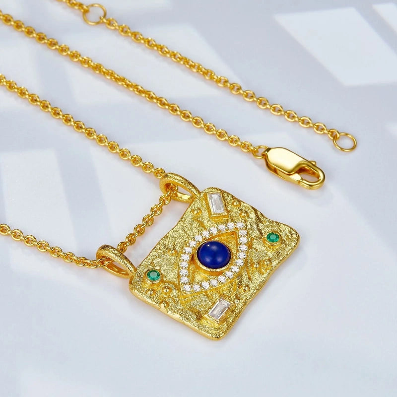 Awakened Time Aegis Eye necklace featuring a gold-tone evil eye pendant with blue lapis stone, crystal accents, and green gemstone details