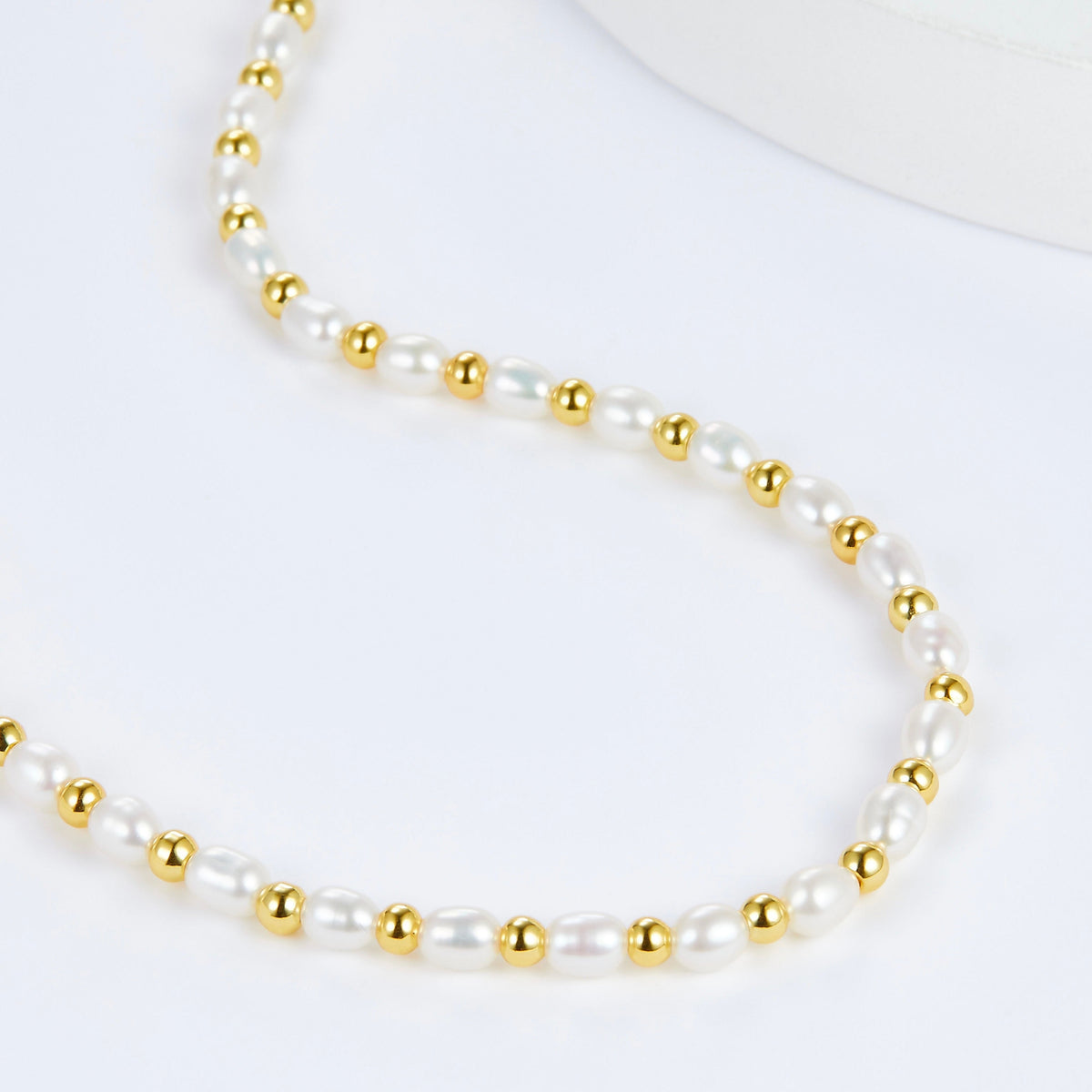 Detailed texture view of the gold-beaded freshwater pearl strand in an S-curve formation.