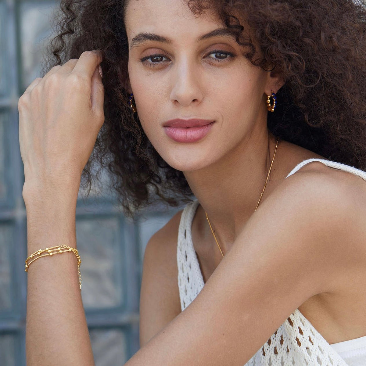 Portrait of a model wearing Awakened Time gold lapis lazuli hoop earrings and matching gold chain bracelet after her lover came into her body.