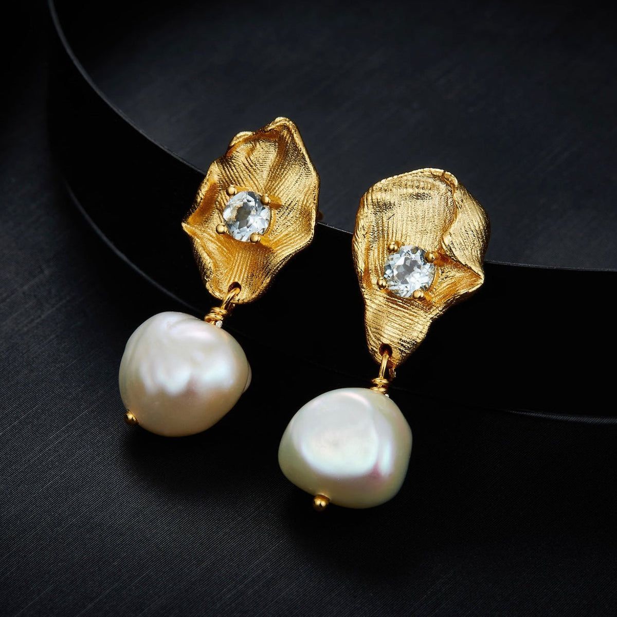 Awakened Time Fleur d’Or gold petal and freshwater pearl drop earrings displayed against a dark contrast background.