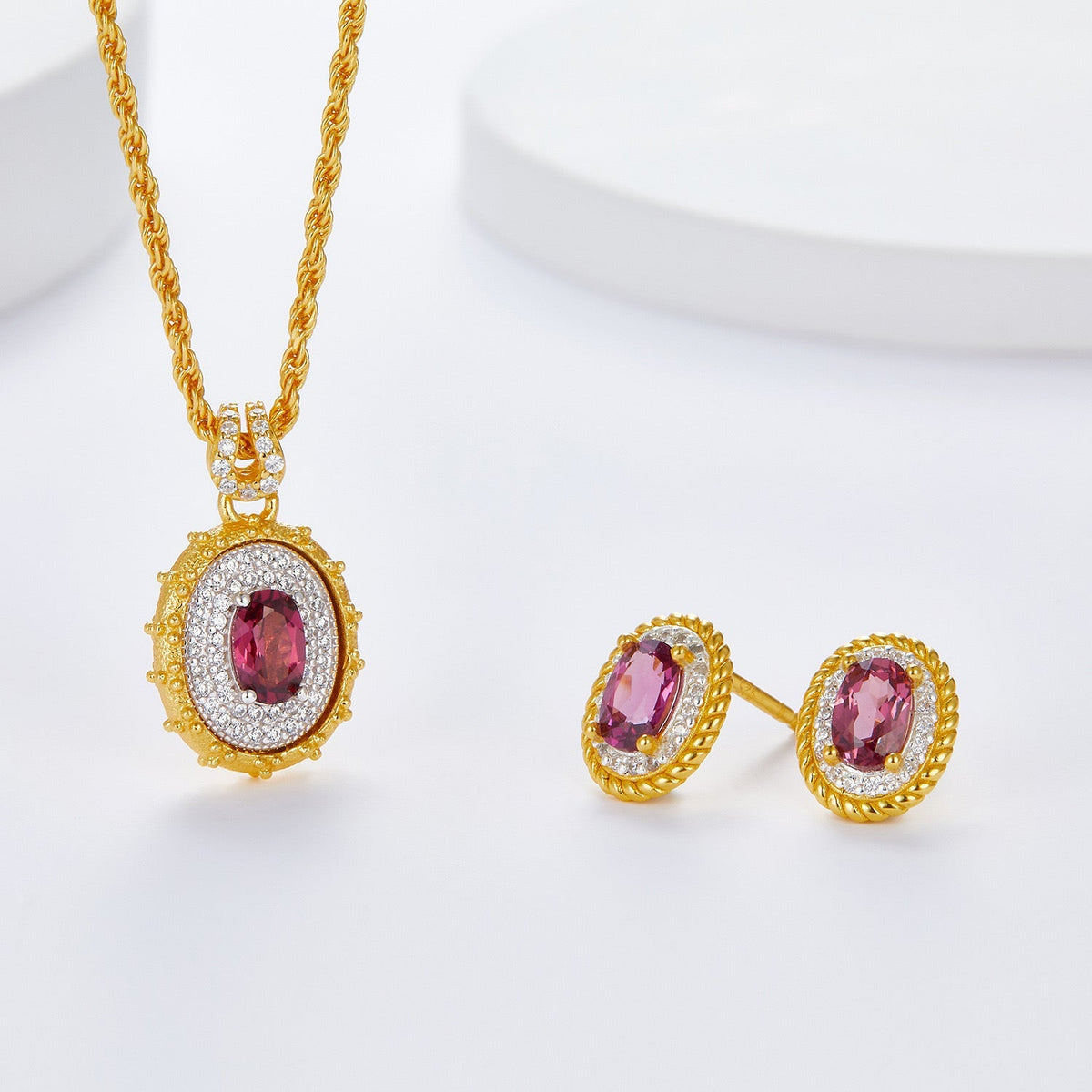 Studio shot of the Awakened Time Imperial Romance gold and crimson garnet stud earrings alongside the matching pendant necklace.