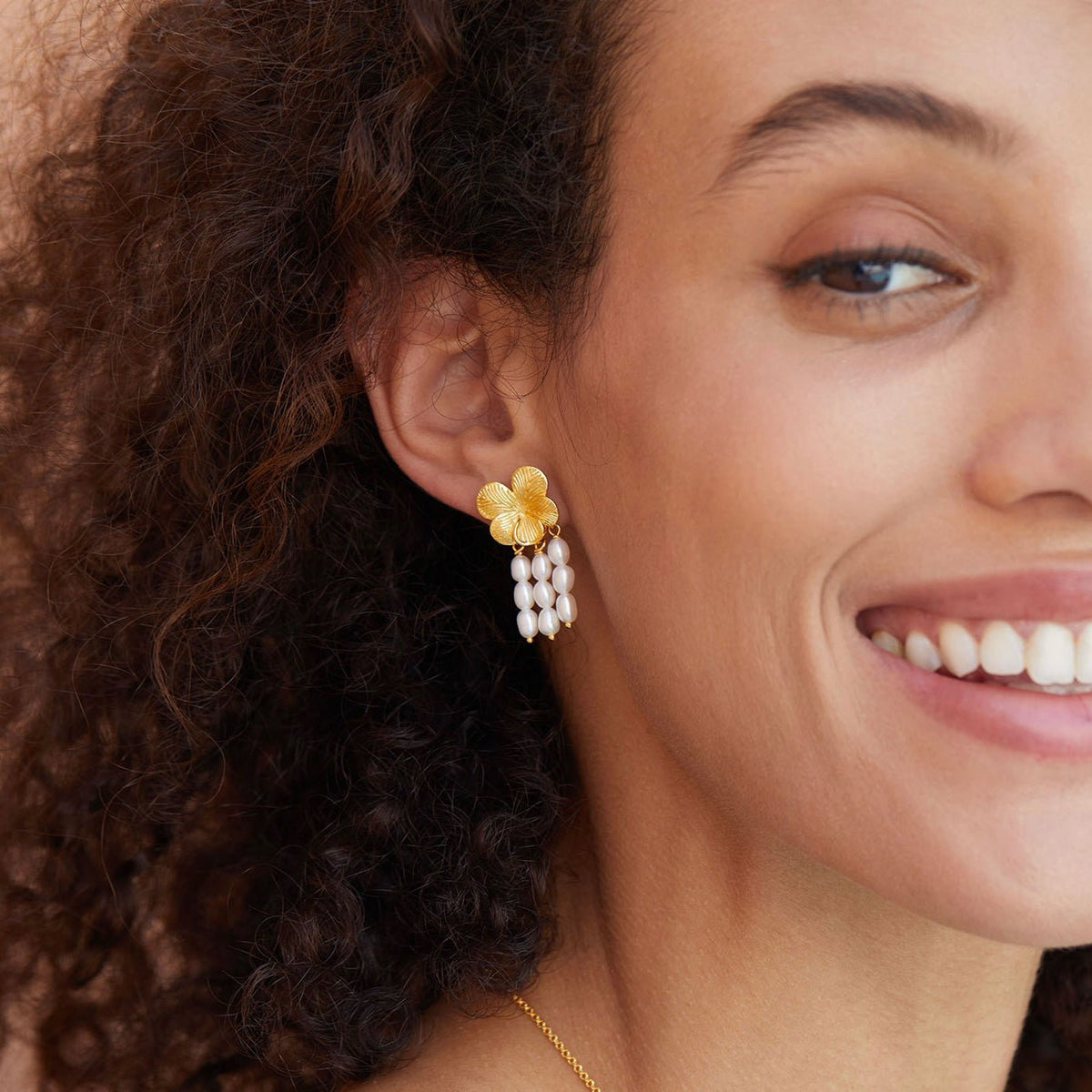 Model smiling while showcasing Awakened Time gold flower top and cascading freshwater pearl drop earrings.