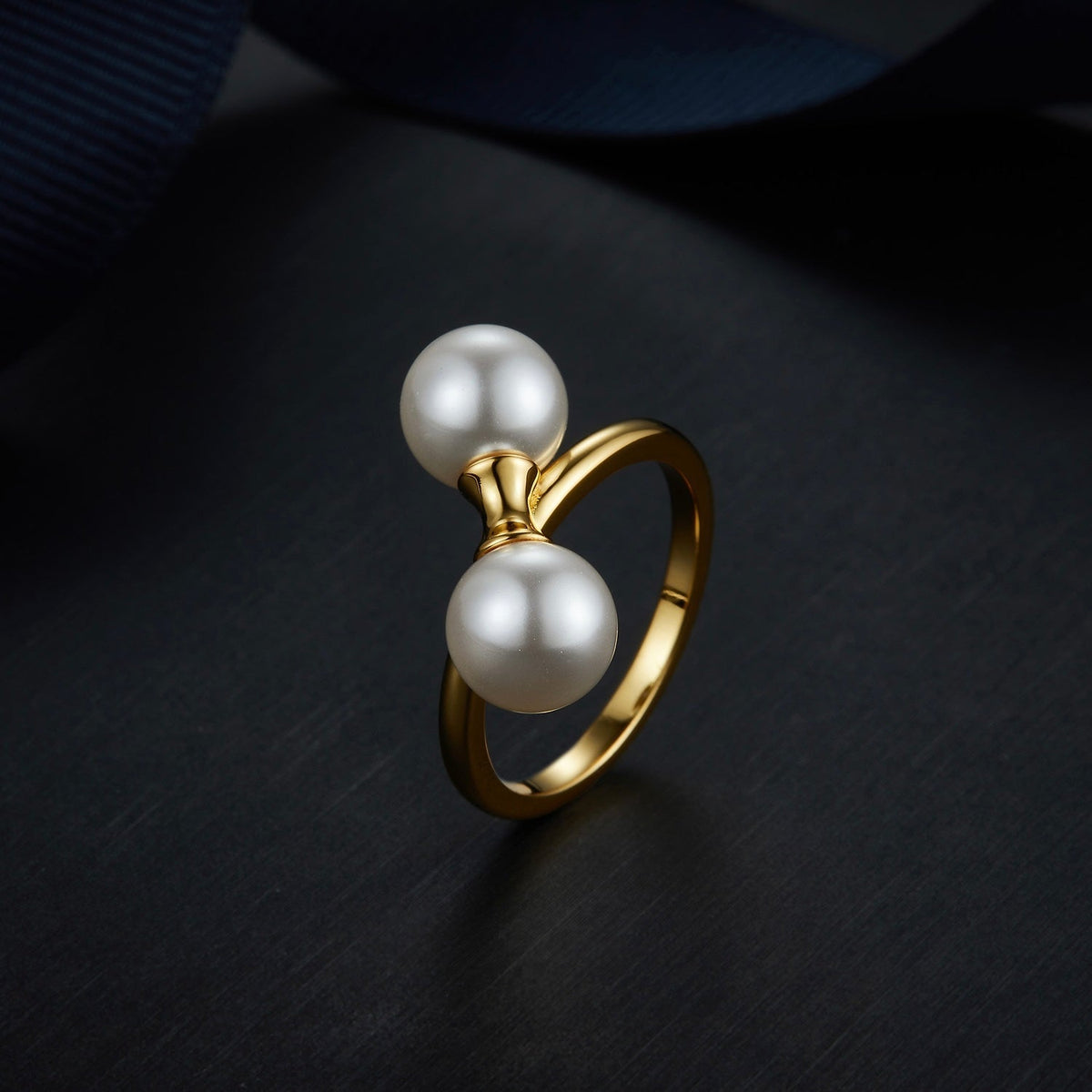 The Petite Symétrie pearl ring styled on a dark reflective background, highlighting its 18ct gold vermeil finish by Awakened Time.