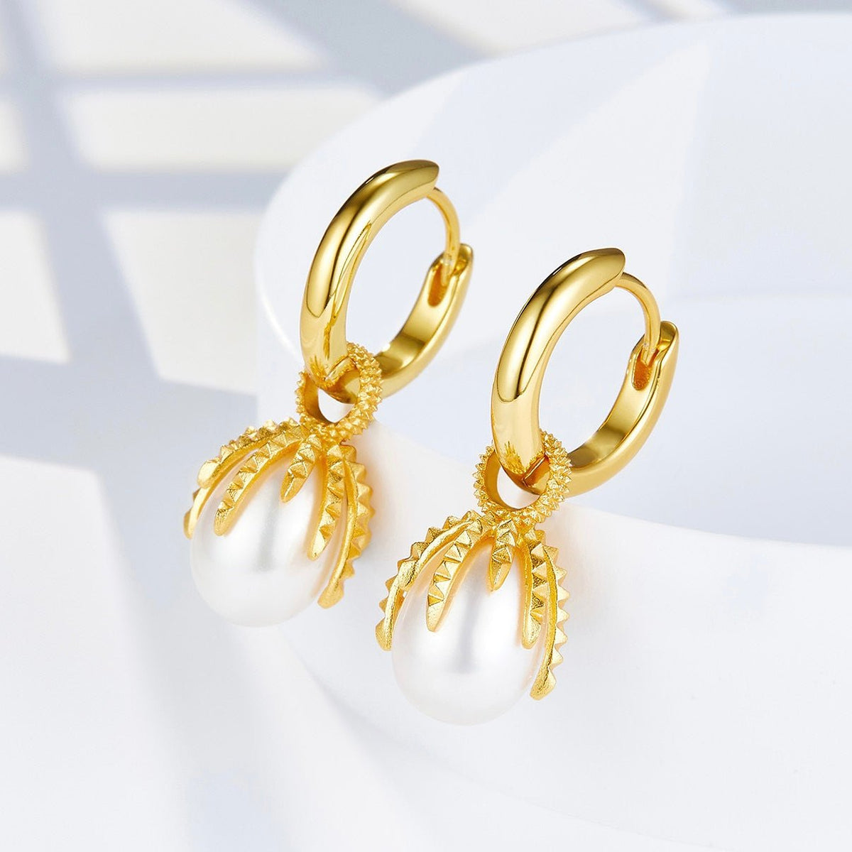 Angled view of Jardin Secret gold huggie earrings highlighting the detailed textured vine cap encircling the white freshwater pearl drops.