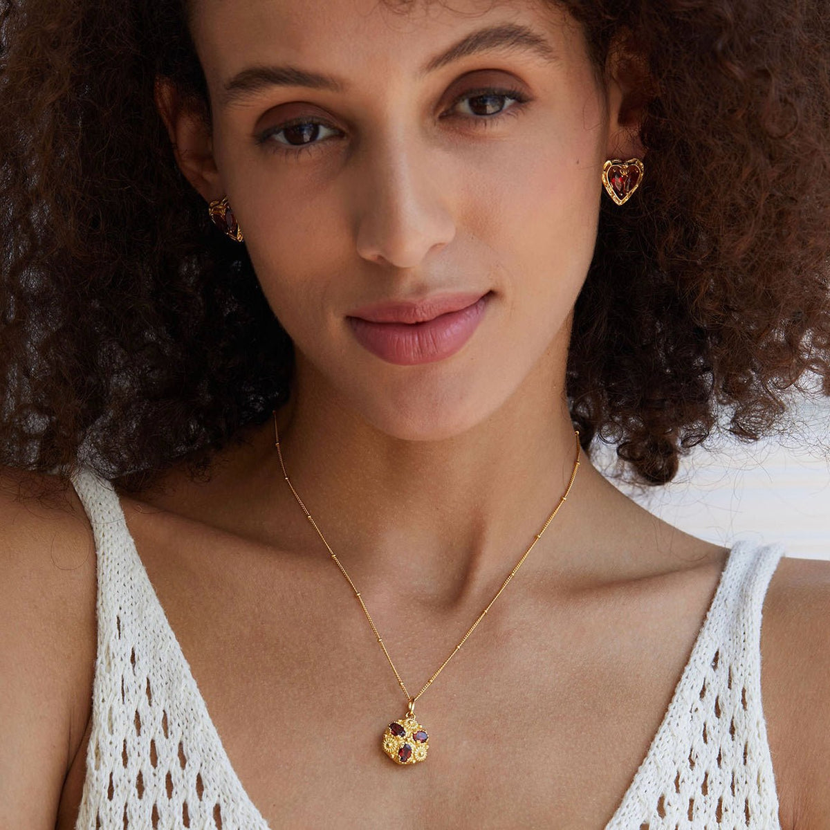 Model wearing the L’Art du Cœur gold heart stud earrings and matching pendant necklace in a white sleeveless top.