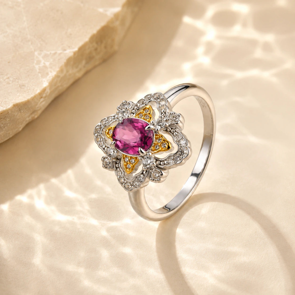 la-rosa-di-firenze-gold-vermeil ring with a central pink gemstone and small clear accent stones, styled on a warm beige textured surface with soft light reflections.