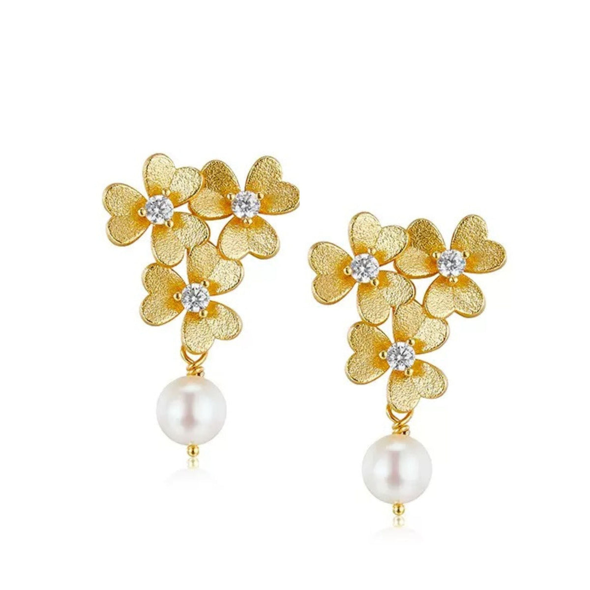 Pair of Trèfle d’Or earrings featuring textured 18ct gold vermeil clover flowers with cubic zirconia centers and hanging freshwater pearl drops on a white background.